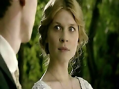 Clemence Poesy lying on her back in sofa as a man kisses her