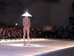 Seductive fashion model in a weird hat walks down the catwalk in the nude